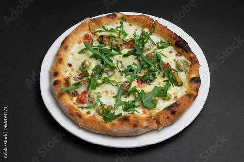 closeup of seafood pizza with shrimp, mussels and arugula on black background