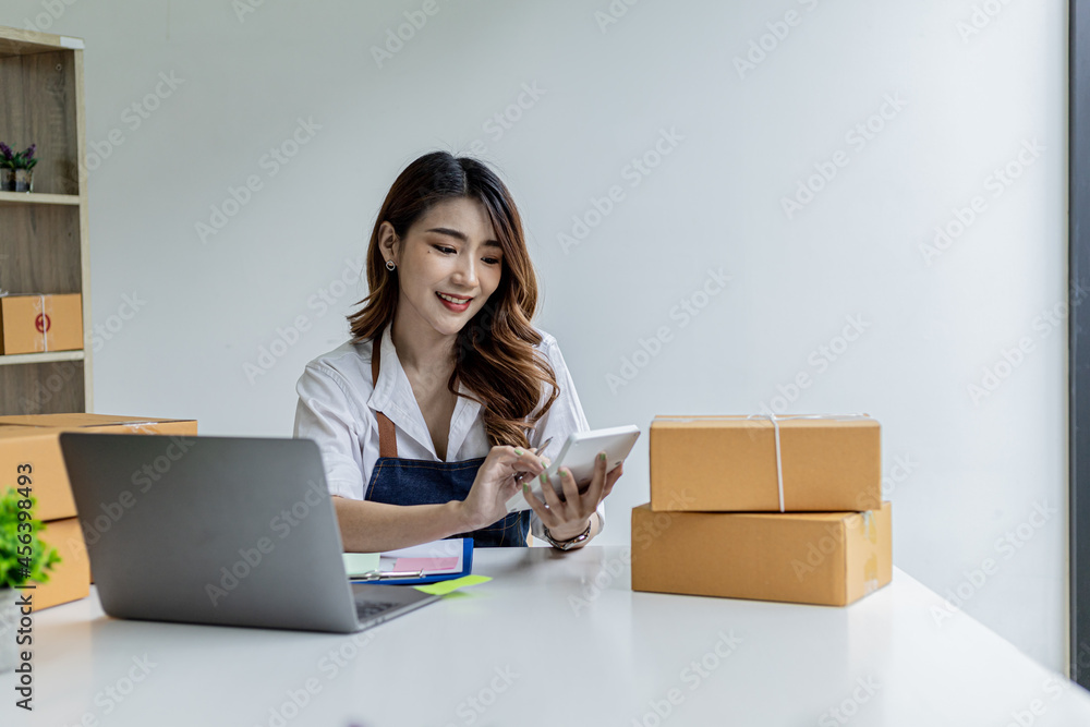 An Asian woman is pressing a white calculator, she owns an online store, she is using an order amount calculator to get a summary of the amount customers have to pay. Online selling concept. An Asian woman is pressing a white calculator, she owns an online store, she is using an order amount calculator to get a summary of the amount customers have to pay. Online selling concept.