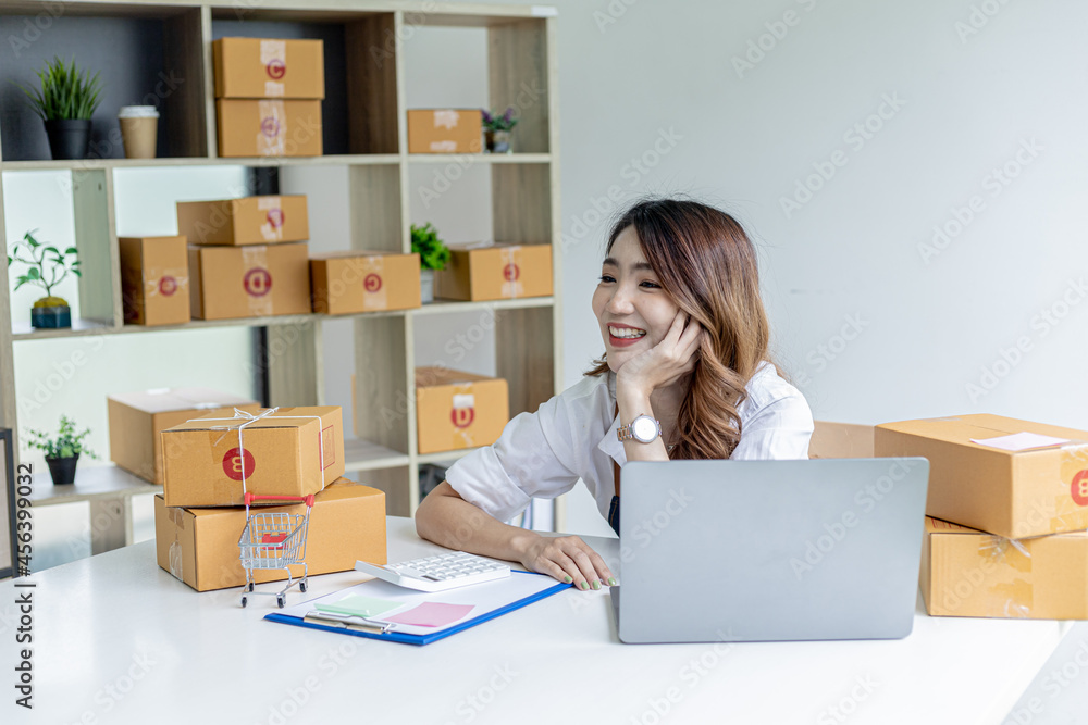 An Asian woman with a happy smile on her face after closing sales targets, she owns an online store, she packs and ships through a private shipping company. Online selling and online shopping concepts An Asian woman with a happy smile on her face after closing sales targets, she owns an online store, she packs and ships through a private shipping company. Online selling and online shopping concepts