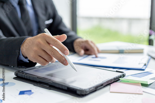 Businessman is using tablet to compare information on financial documents, he is checking company financial documents in office, company financial statements. Concept of financial management.