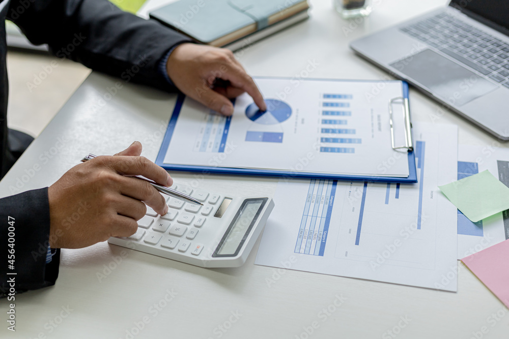 Close-up of a business man using a white calculator, a financial businessman examining the numerical data on a company financial document, He uses a calculator to verify the accuracy of numbers. Close-up of a business man using a white calculator, a financial businessman examining the numerical data on a company financial document, He uses a calculator to verify the accuracy of numbers.