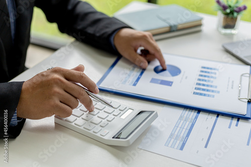 Close-up of a business man using a white calculator, a financial businessman examining the numerical data on a company financial document, He uses a calculator to verify the accuracy of numbers.