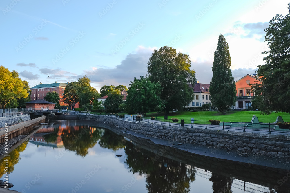 Fototapeta premium The view of river banks, lawn and old buildings in the center of small old Swedish town Vasteras shot in the evening on clear September day
