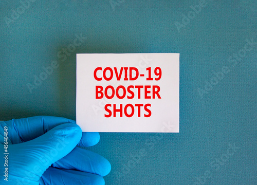 Covid-19 booster shots vaccine symbol. White note with words Covid-19 booster shots, beautiful blue background, doctor hand in blue glove. Covid-19 booster shots vaccine concept.