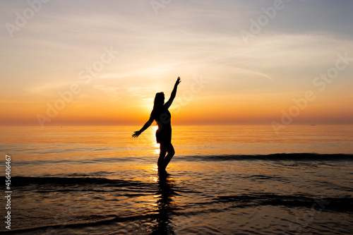 A woman silhouette standing in the calm sea during sunset.