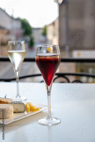 Drinking of Kir Royal, French aperitif cocktail made from creme de cassis topped with champagne, typically served in flute glass, with view on old French village