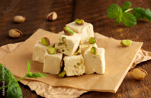 Traditional oriental dessert Chekme. Halva with pistachios on parchment paper on a wooden background. Natural vegan product. Turkish, Arab and Jewish national sweets.