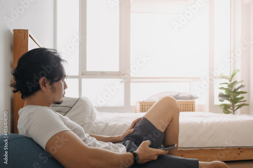 Asian man feels relax and using smartphone in his apartment.