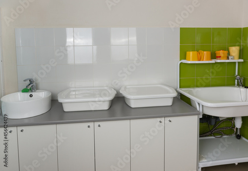 Sink and enameled containers for washing and disinfection in the clinic room for processing reusable medical equipment and instruments. Containers with disinfectant and a timer on the shelf