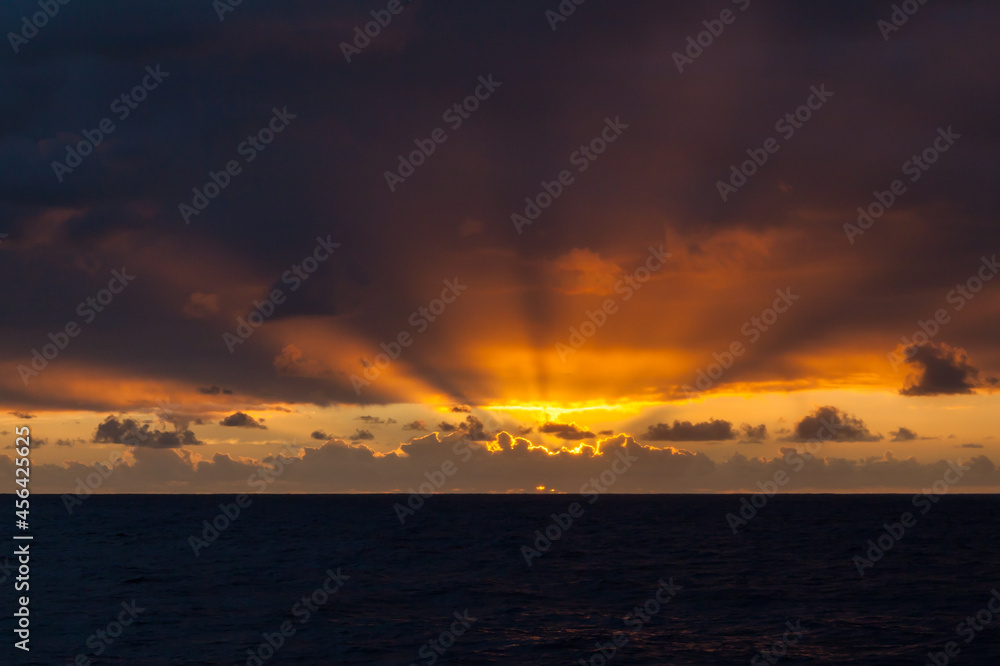 sunset on open ocean against the backdrop of clouds with the sun's rays breaking through