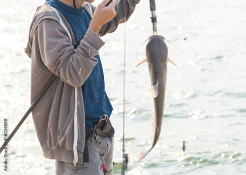 Asian fisherman with rod and fish lip gripper handle the catfish near Lavon Lake, Texas, USA photo