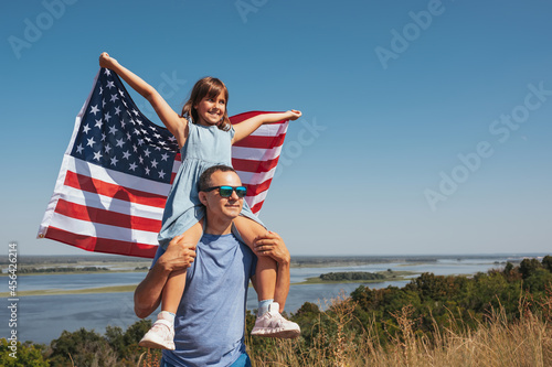 Happy family father and daughter having fun with America flag at sunset outdoors