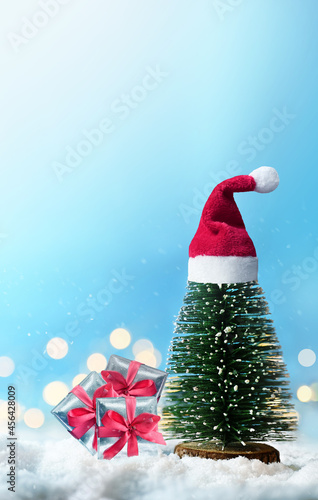 Christmas tree with Santa hat and gift box on snow. Christmas concept.