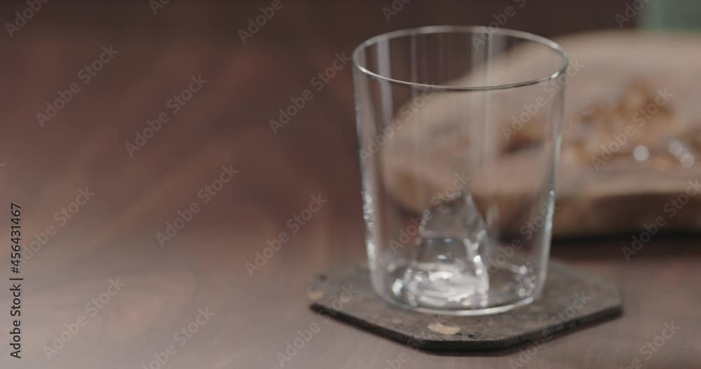 Slow motion man put ice into tumbler glass on walnut table Slow motion man put ice into tumbler glass on walnut table