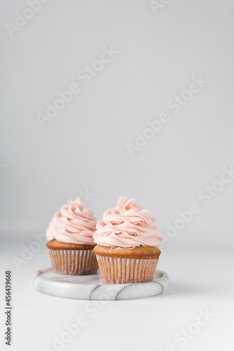 Vanilla cupcake with a tall swirl of pink frosting, plain cupcake with pastel pink buttercream