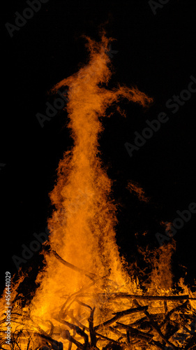 VERTICAL: Scenic shot of a blazing campfire rising into dark summer night sky.
