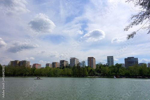 Titan park in Bucharest with blocks of apartments on the lake's shore and white clouds on the sky in spring 