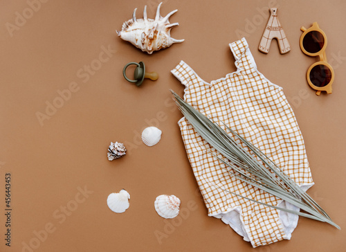 Cute retro swimsuit for baby girl with seashells and beach accessories on brown background. Summer holiday concept. Top view, flat lay photo