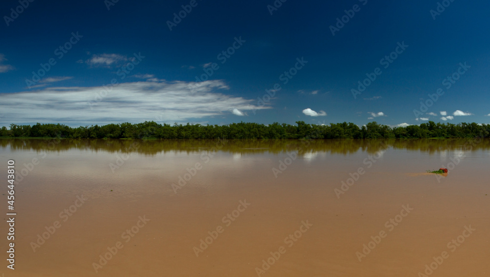 Symmetry in nature. Panorama view of the brown water Parana river under a clear blue sky. View of the wide river and jungle reflection in the water.