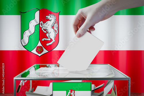 North Rhine-Westphalia flag, hand dropping ballot card into a box - voting/ election in Germany concept - 3D illustration