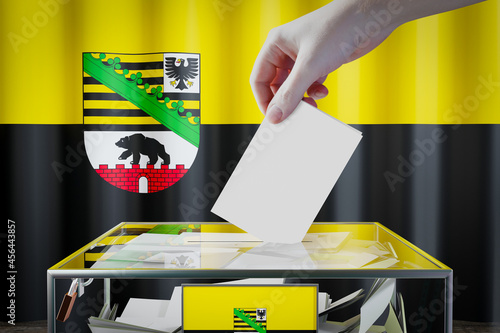 Saxony-Anhalt flag, hand dropping ballot card into a box - voting/ election in Germany concept - 3D illustration photo