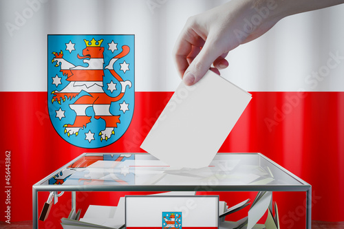 Thuringia flag, hand dropping ballot card into a box - voting/ election in Germany concept - 3D illustration