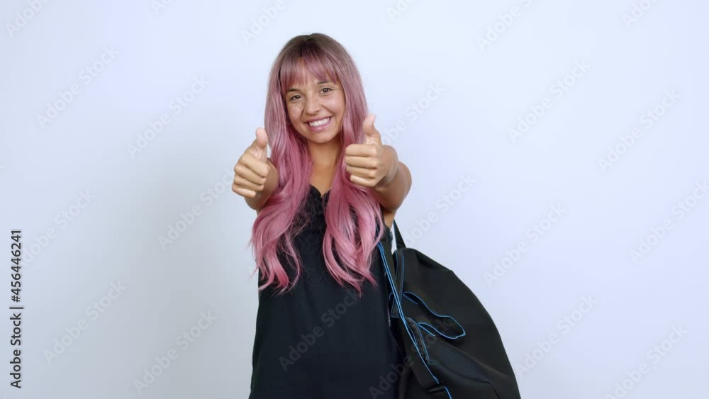 Young woman with pink hair with sport bag giving thumbs up and smiling because something good has happened over isolated background Young woman with pink hair with sport bag giving thumbs up and smiling because something good has happened over isolated background