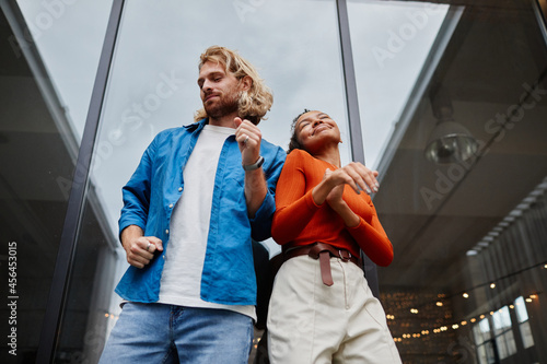 Low angle portrait of colorful young couple dancing at rooftop under sky, copy space