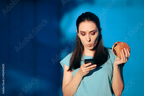 Slika na platnu Woman Checking Smartphone in her Lunch Break Holding a Burger