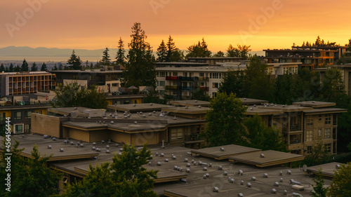 Tangerine sunset over mid-rise condominiums nestled among trees at Univercity Highlands residential development on Burnaby Mountain, BC
