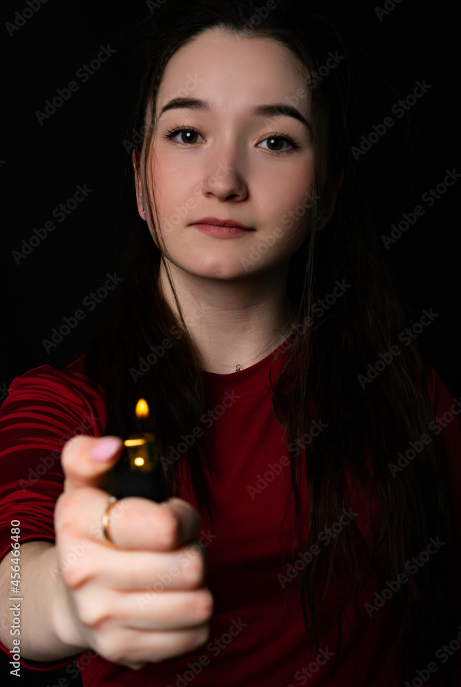 Obraz premium portrait of a girl. close-up. model in a red t-shirt, holding a fire, looking at the camera. Black background.