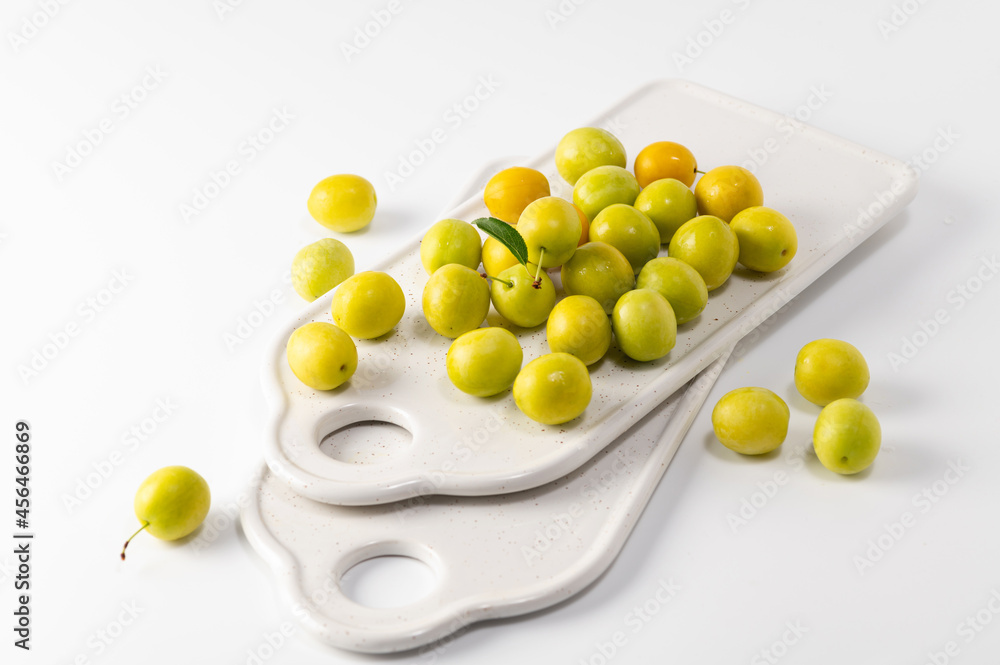 yellow freshly torn cherry plum, ceramic boards for serving on a white background yellow freshly torn cherry plum, ceramic boards for serving on a white background