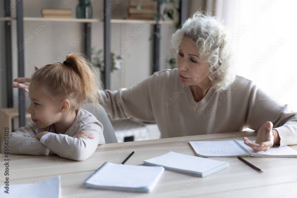 Worrying older mature grandmother talking to upset small granddaughter, stuck with hard task, feeling stressed while studying at home or preparing for exams, learning problems, education concept. Worrying older mature grandmother talking to upset small granddaughter, stuck with hard task, feeling stressed while studying at home or preparing for exams, learning problems, education concept.