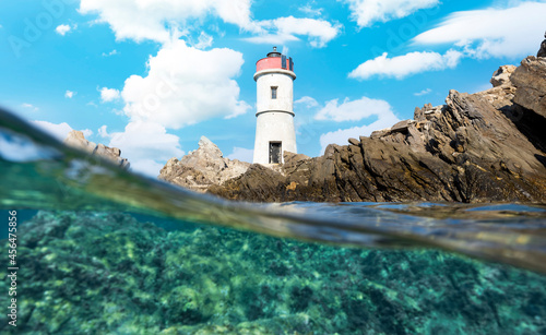 (Selective focus) Split shot, over under shot. Half sky, half underwater. Defocused waves in the foreground with a lighthouse on a rocky coast. Faro di Capo Ferro, Sardiinia, Italy.