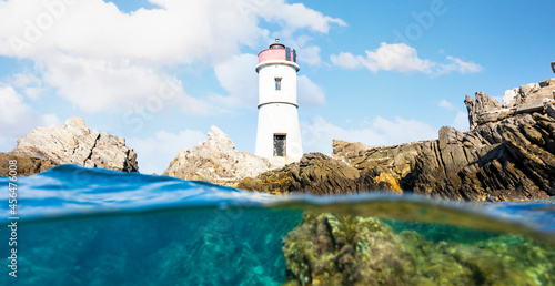 (Selective focus) Split shot, over under shot. Half sky, half underwater. Defocused waves in the foreground with a lighthouse on a rocky coast. Faro di Capo Ferro, Sardiinia, Italy. photo