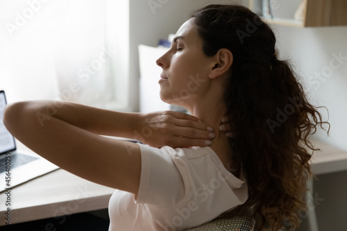 Woman touch stiff neck, experiencing sore shoulders and severe back problems, feels ache muscles from long sedentary work at laptop side rear close up. Fibromyalgia, need exercise, treatment concept