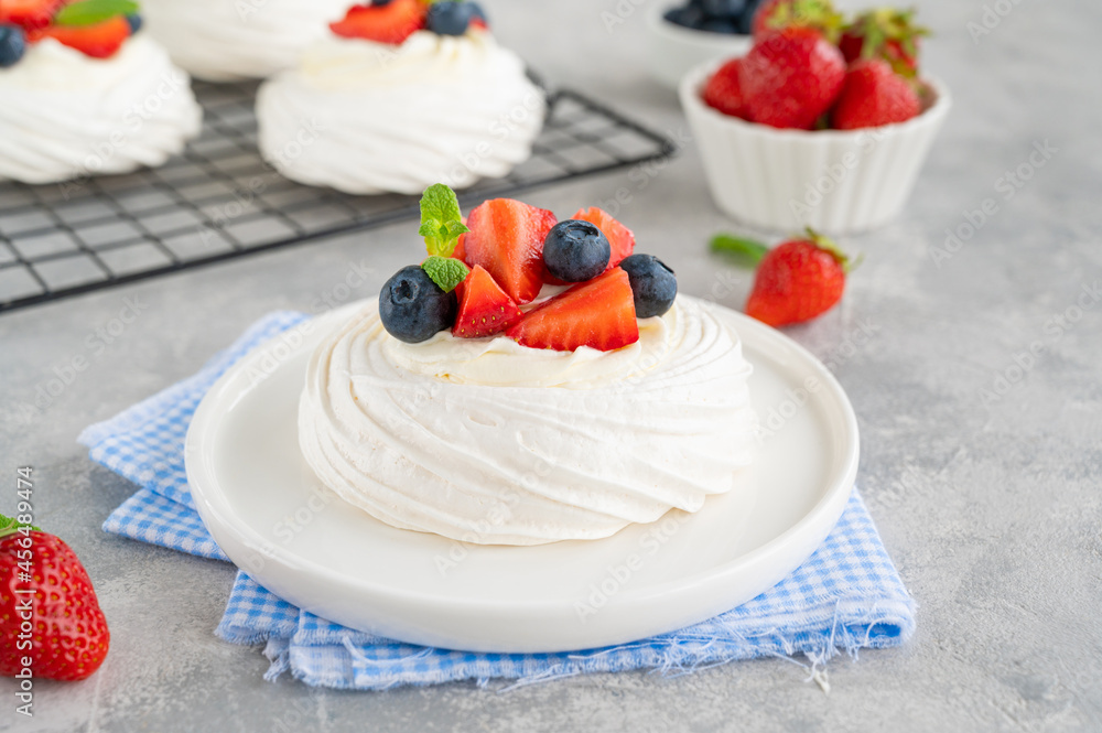 Pavlova meringue cake with whipped cream and fresh berries on top on a plate on a gray concrete background. Summer dessert. Copy space. Pavlova meringue cake with whipped cream and fresh berries on top on a plate on a gray concrete background. Summer dessert. Copy space.