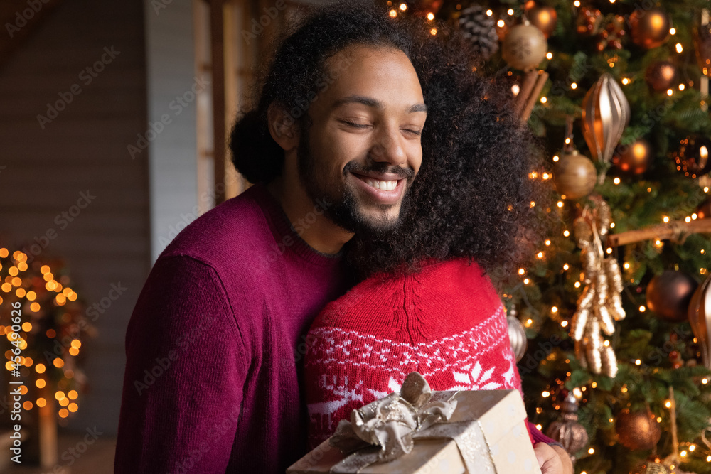 Happy grateful African American young man hug biracial woman celebrate New Year winter holidays together. Smiling loving ethnic couple embrace exchange gifts presents on Christmas Eve. Happy grateful African American young man hug biracial woman celebrate New Year winter holidays together. Smiling loving ethnic couple embrace exchange gifts presents on Christmas Eve.
