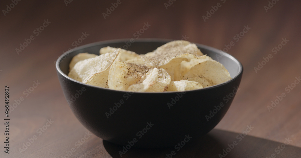ground black pepper fall on potato chips fall in black bowl on walnut table