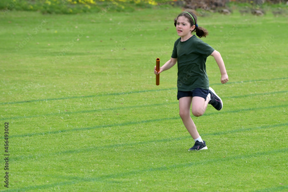 Fast and strong young girl (female age 07-08) running relay race on grass running track outdoors.