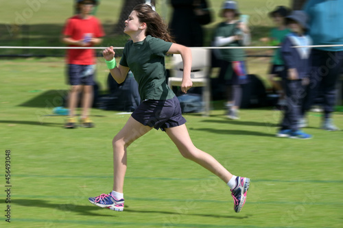 Motion blur of a young girl (female age 11-12) running fast on grass running track outdoors.