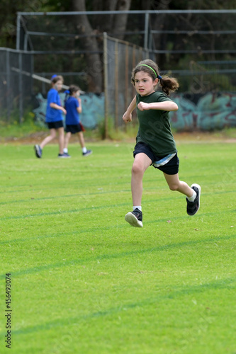 Determent young girl (female age 07-08) running relay race on grass running track outdoors.