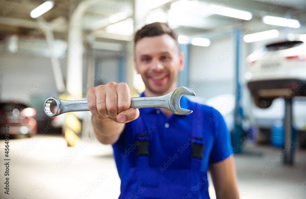 Close up photo of happy auto mechanics with an open-end wrench in hand on the background of repairing a car Close up photo of happy auto mechanics with an open-end wrench in hand on the background of repairing a car