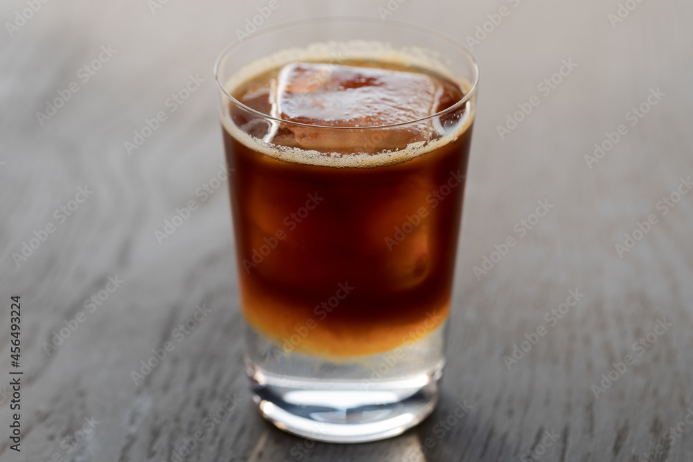Espresso tonic with clear ice cube in tumbler glass on oak wood table with copy space