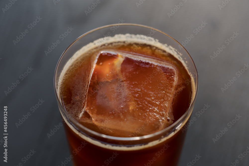 Closeup espresso tonic with clear ice cube in tumbler glass on oak wood table Closeup espresso tonic with clear ice cube in tumbler glass on oak wood table