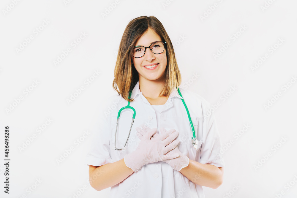 Studio portrait of young female doctor posing on white background, holding hands on chest next to heart, thank you sign Studio portrait of young female doctor posing on white background, holding hands on chest next to heart, thank you sign