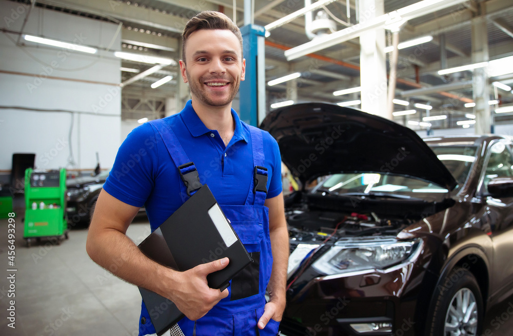 Confident and concentrated young and experienced car repair specialist with a tablet in his hand inspects and diagnosis the car for breakdowns Confident and concentrated young and experienced car repair specialist with a tablet in his hand inspects and diagnosis the car for breakdowns