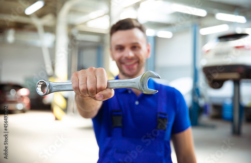 Close up photo of happy auto mechanics with an open-end wrench in hand on the background of repairing a car