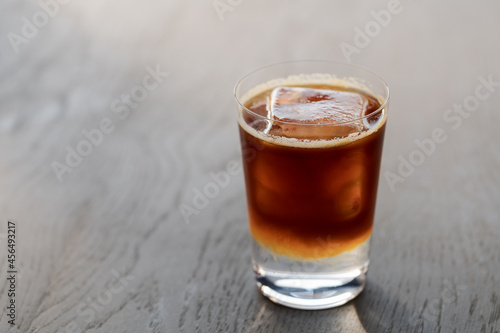 Espresso tonic with clear ice cube in tumbler glass on oak wood table with copy space