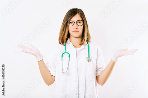 Studio portrait of young female doctor with clueless and confused fasial expression  spreading arms to the different sides
